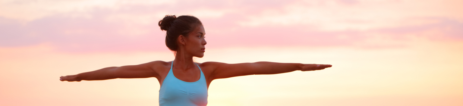 Yoga woman in zen meditating in warrior pose relaxing outside by beach at sunrise or sunset.