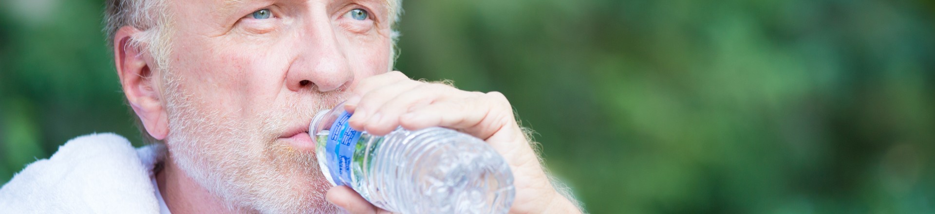 man drinking from water bottle after exercising outdoors