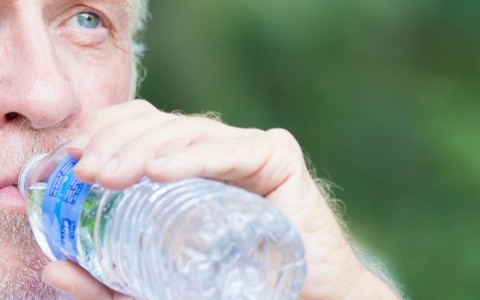 man drinking from water bottle after exercising outdoors