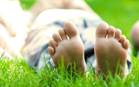 three kids laying in the grass with barefeet