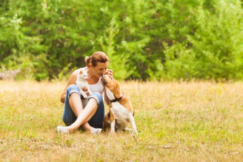 woman sits with her dog and cat in a field and they use natural flea and tick prevention methods